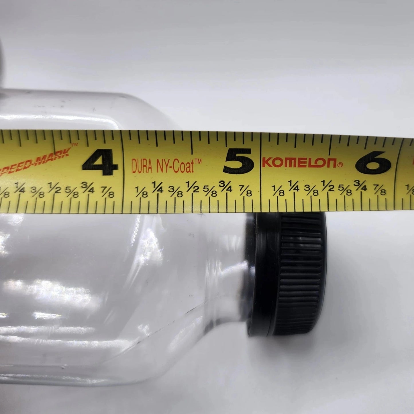 Clear bottle with black cap being measured by a yellow tape measure on a white background