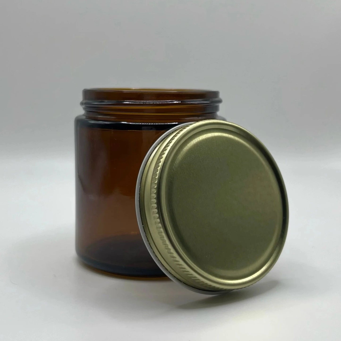 Amber glass jar with a gold metal lid on a white background