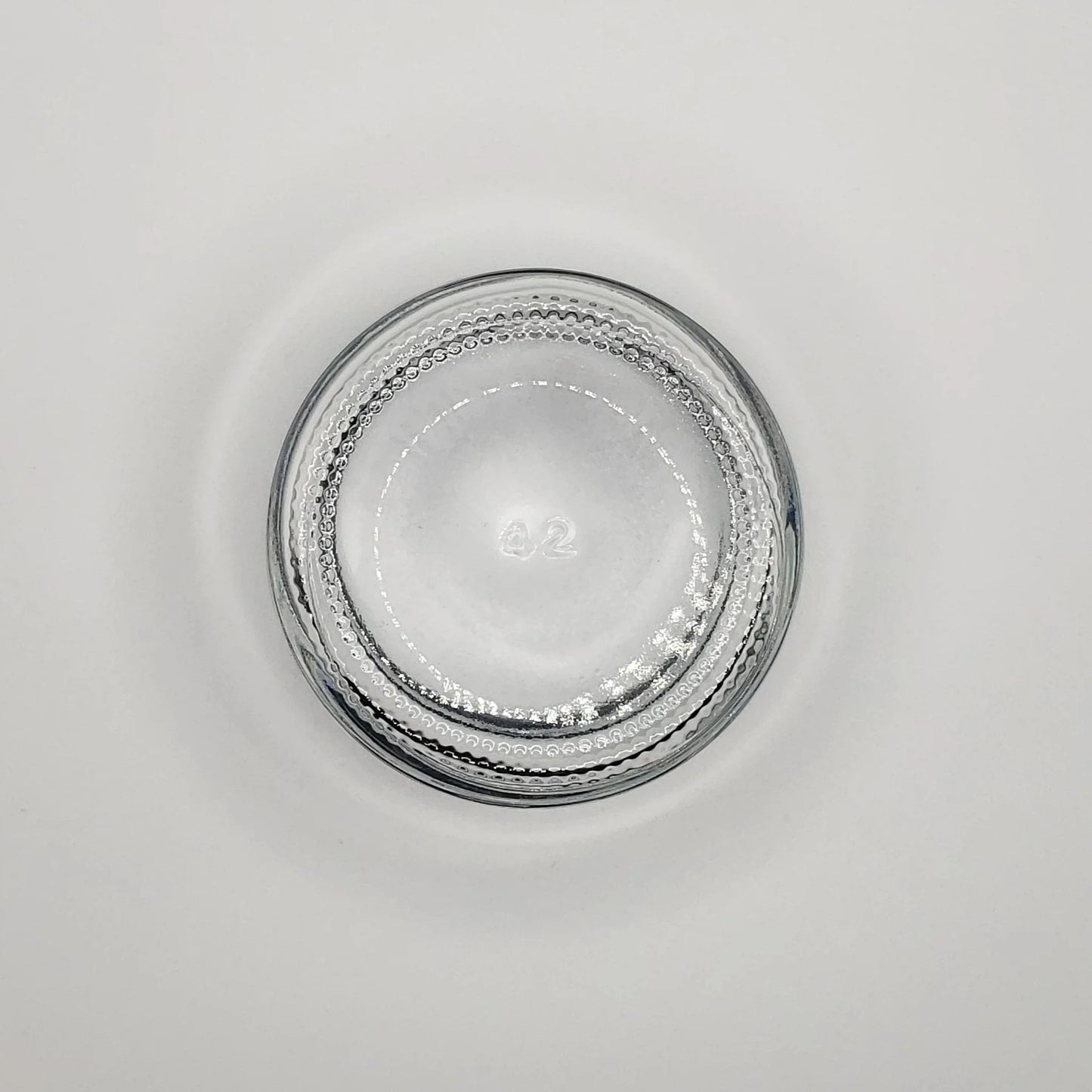 Round 2 ounce glass jar with textured rim on a light gray background