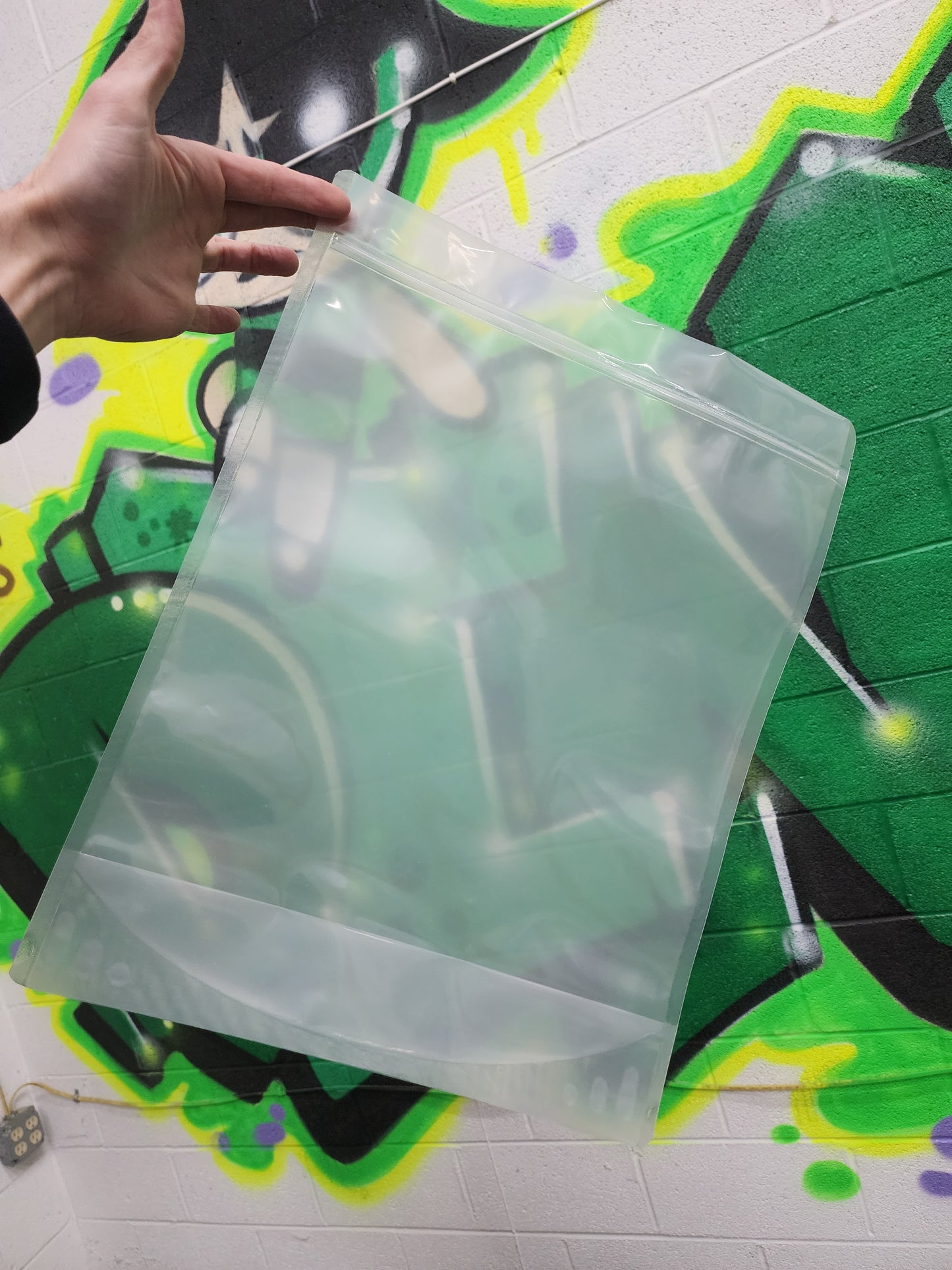 Clear size P mylar bag held by a hand against a colorful background
