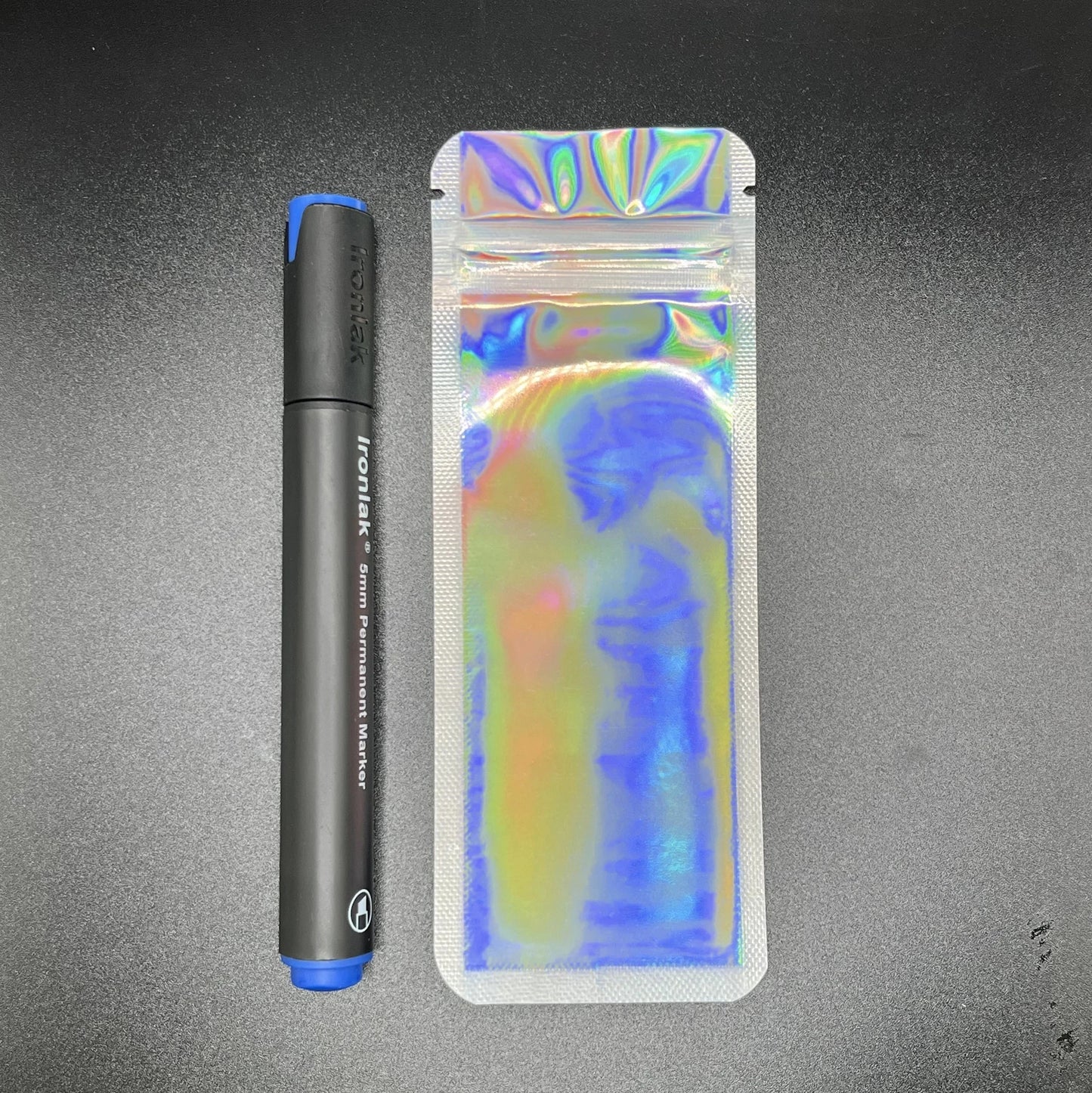 Silver holographic device bag next to a black marker on a black background