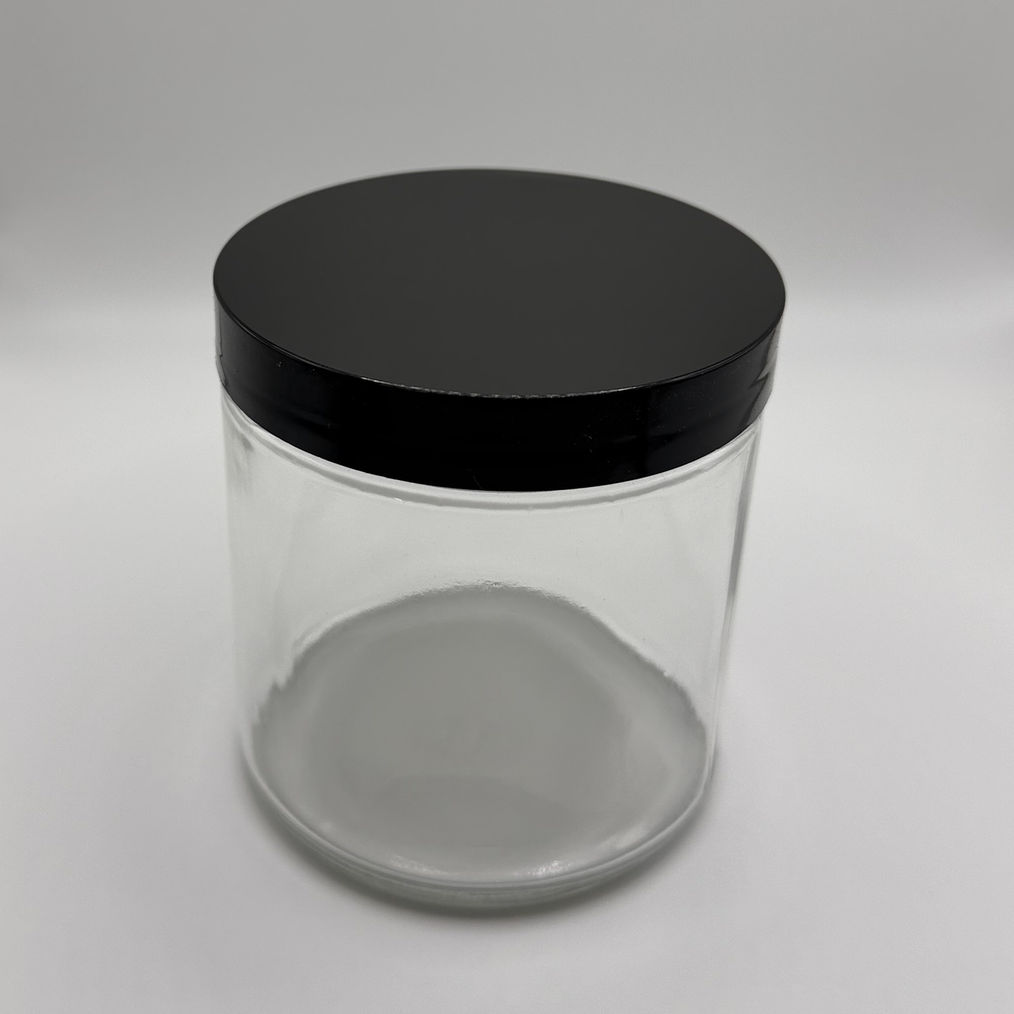 16oz glass jar with a black plastic lid on a white background
