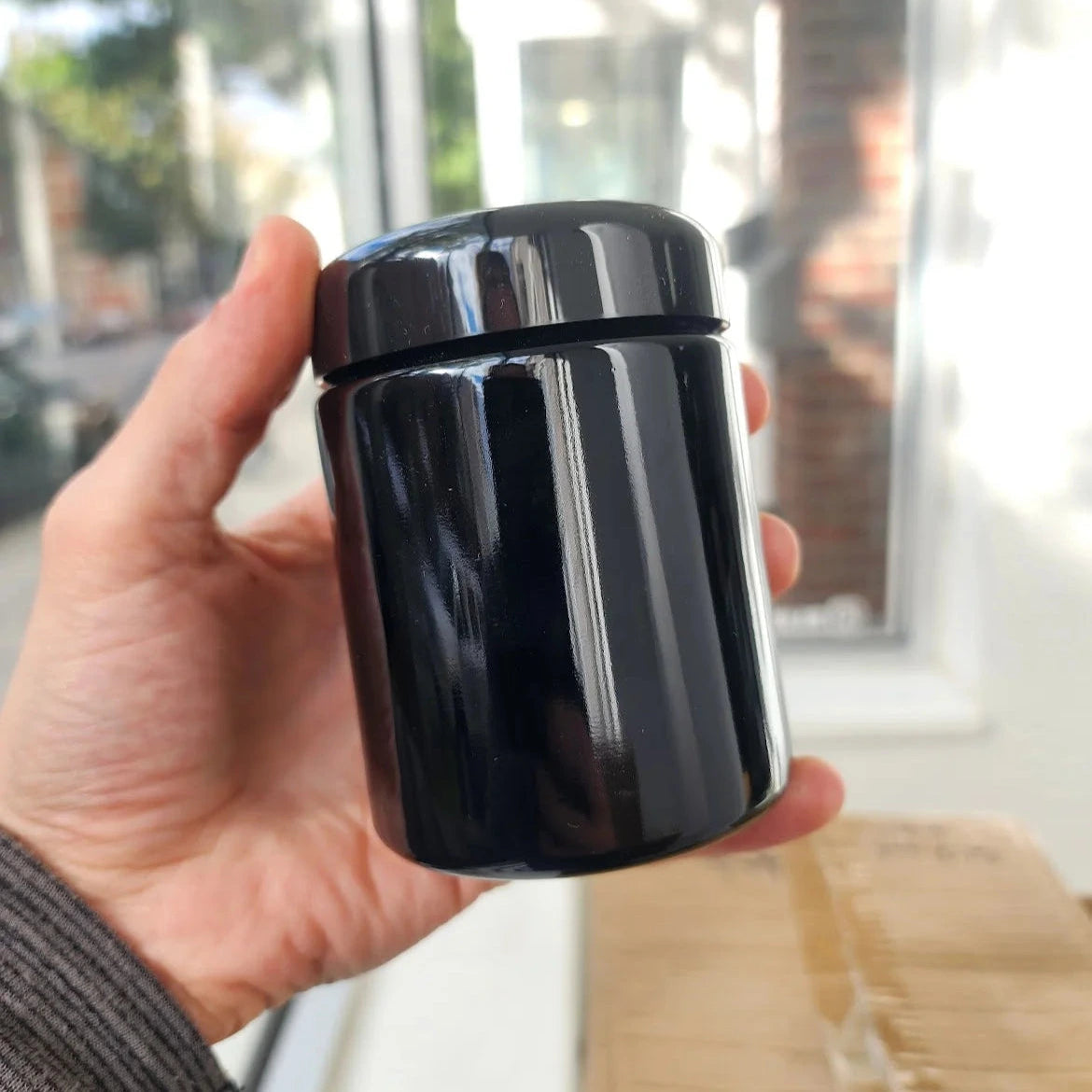 Person holding a black cylindrical glass jar