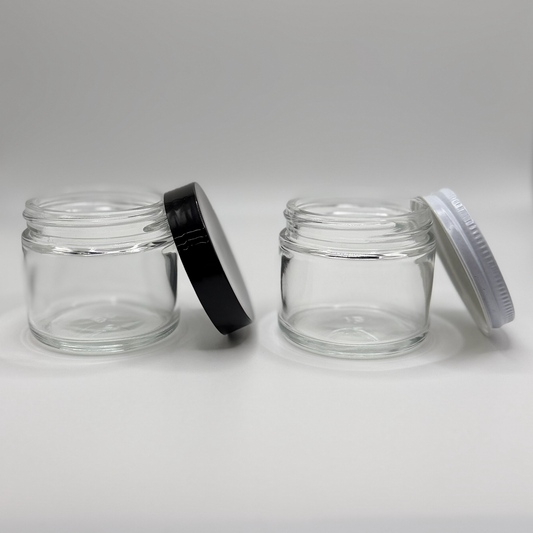 Two 2oz glass jars with a white tin lid and a black plastic lid on a white background