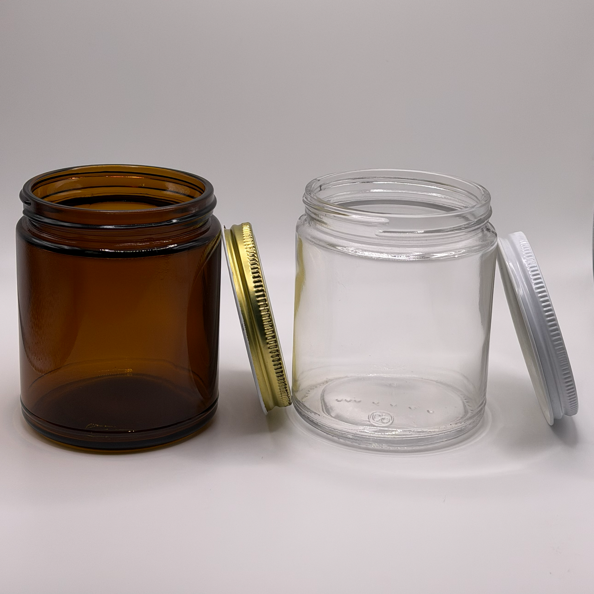 Amber 9oz glass jar with a gold tin lid next to a clear 9oz glass jar with a white tin lid