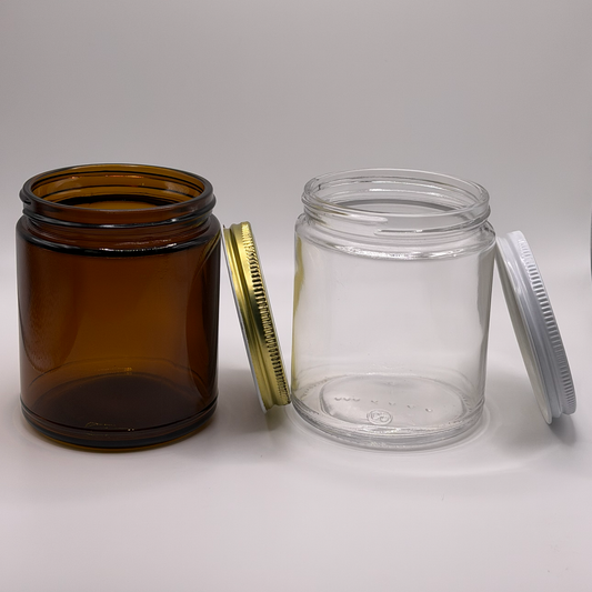 Amber 9oz glass jar with a gold tin lid next to a clear 9oz glass jar with a white tin lid