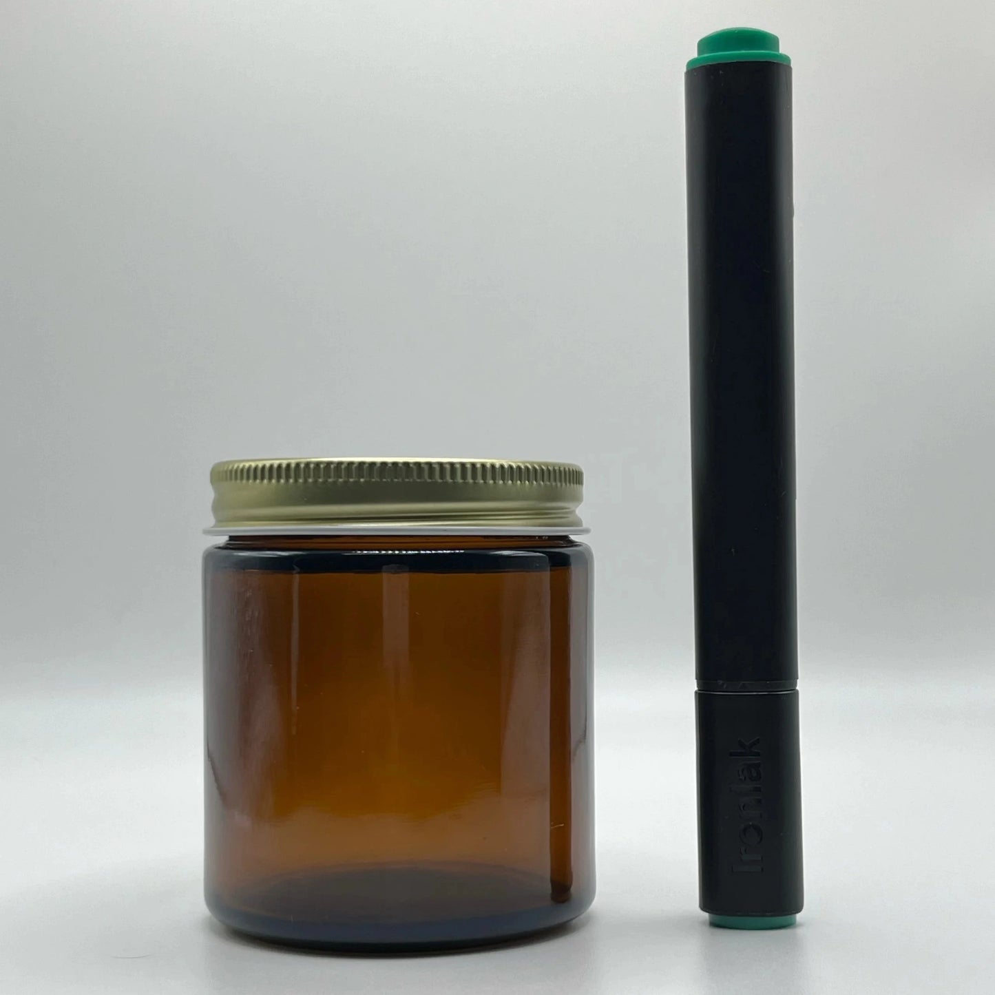Amber glass jar with a metal lid and a black cylindrical object on a white background