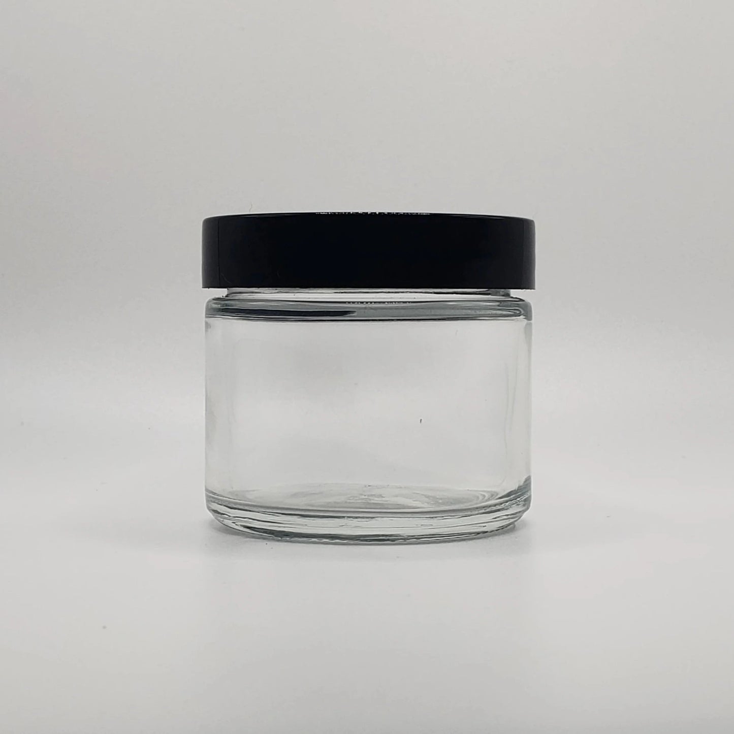 Clear glass jar with a black lid on a light gray background