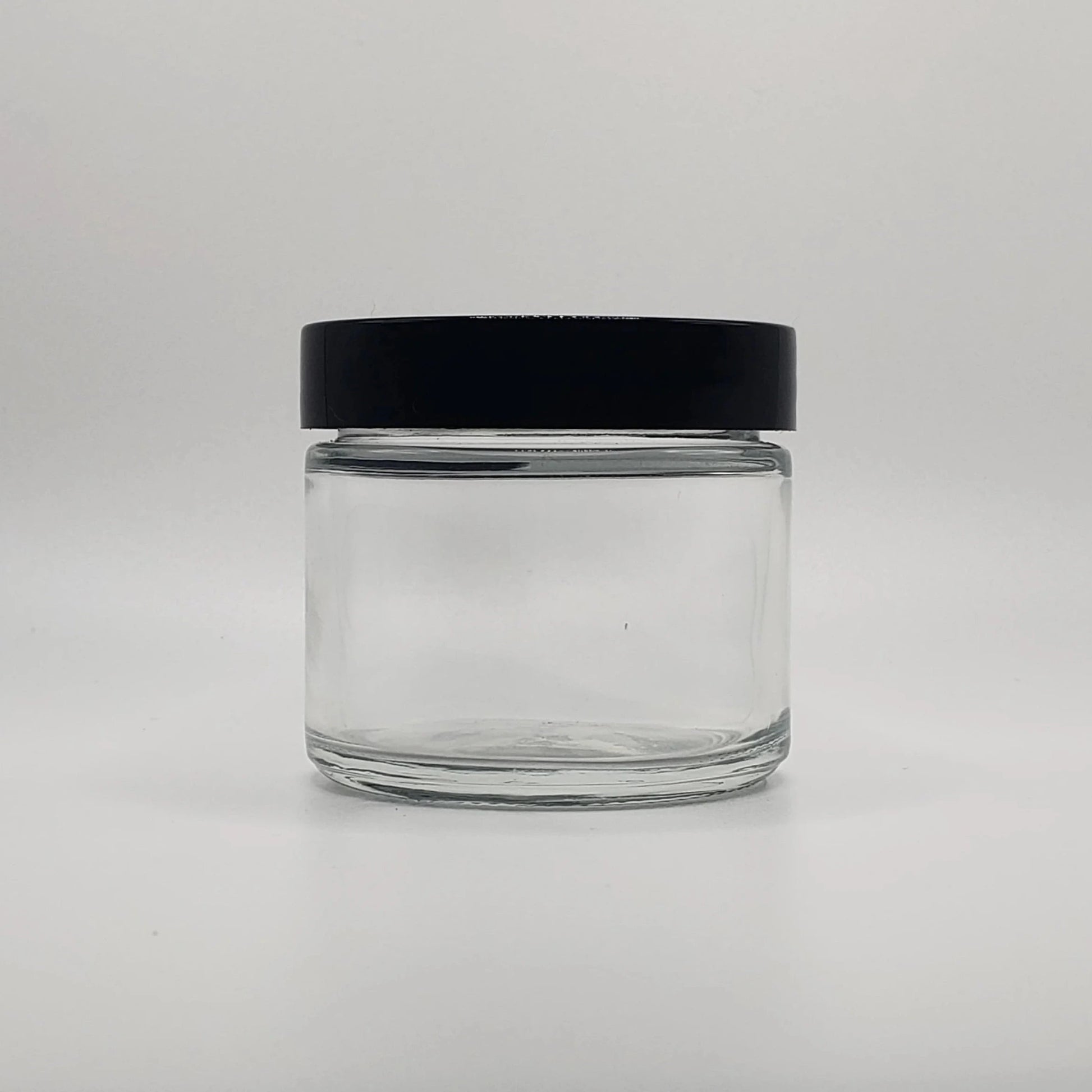 Clear glass jar with a black lid on a light gray background