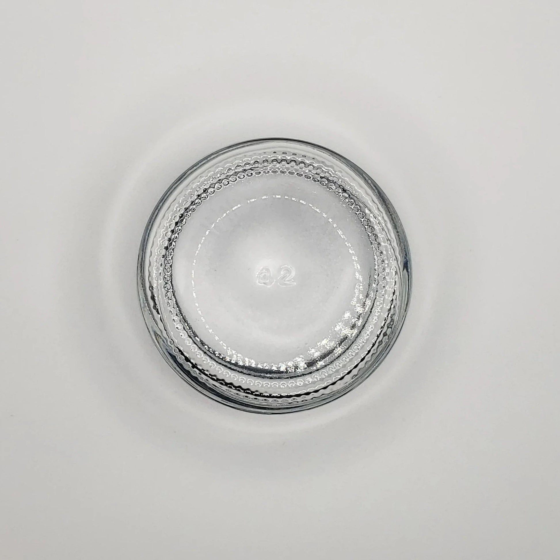 Round 2 ounce glass jar with textured rim on a light gray background