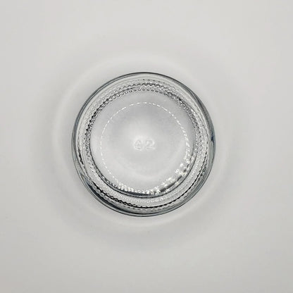 Round 2 ounce glass jar with textured rim on a light gray background