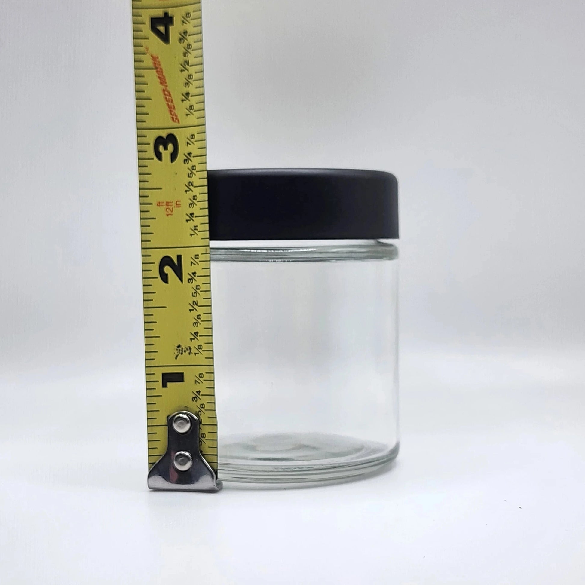 Clear glass jar with black lid and measuring tape on a white background