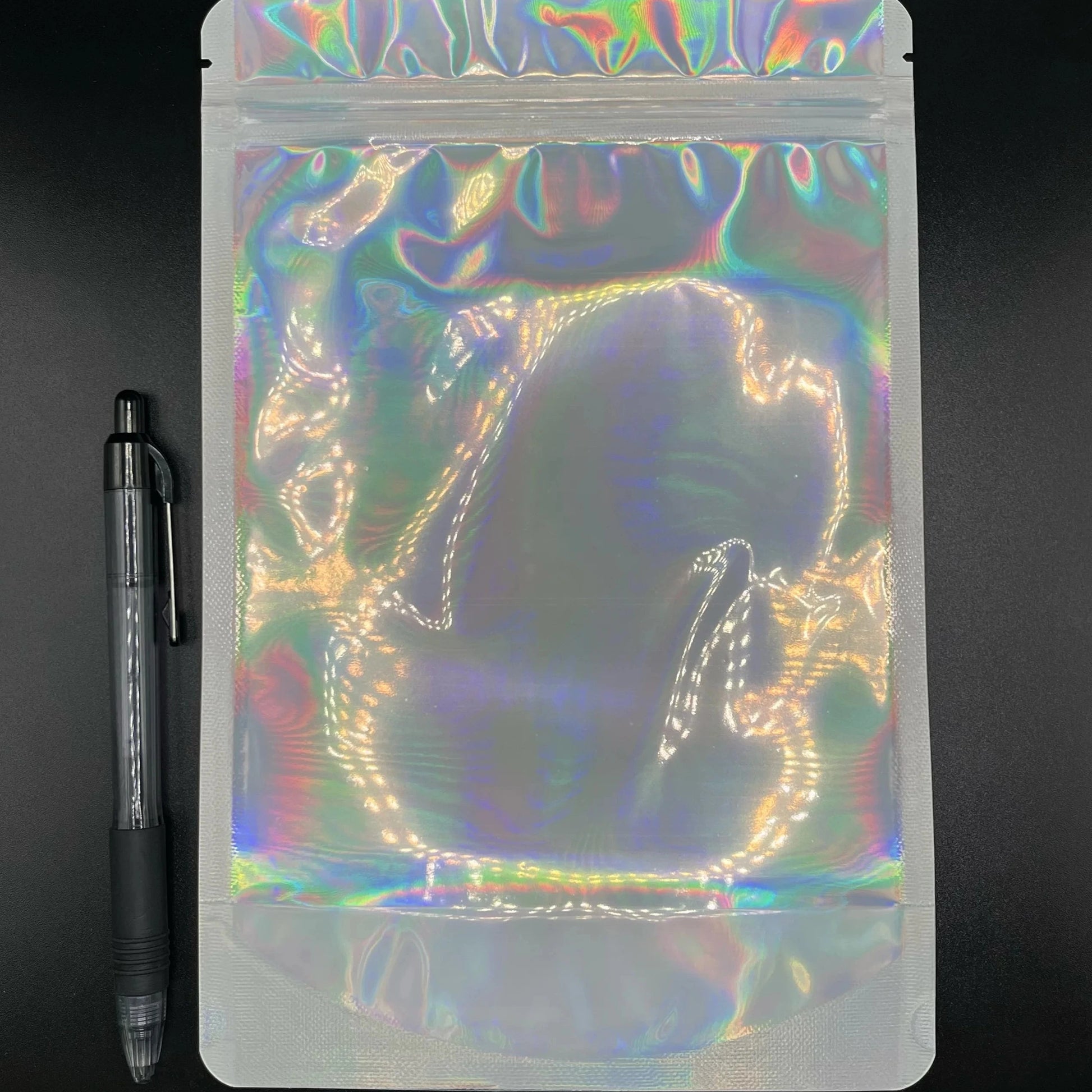 6x9 Laser Black/Clear mylar bag next to a pen on a black background