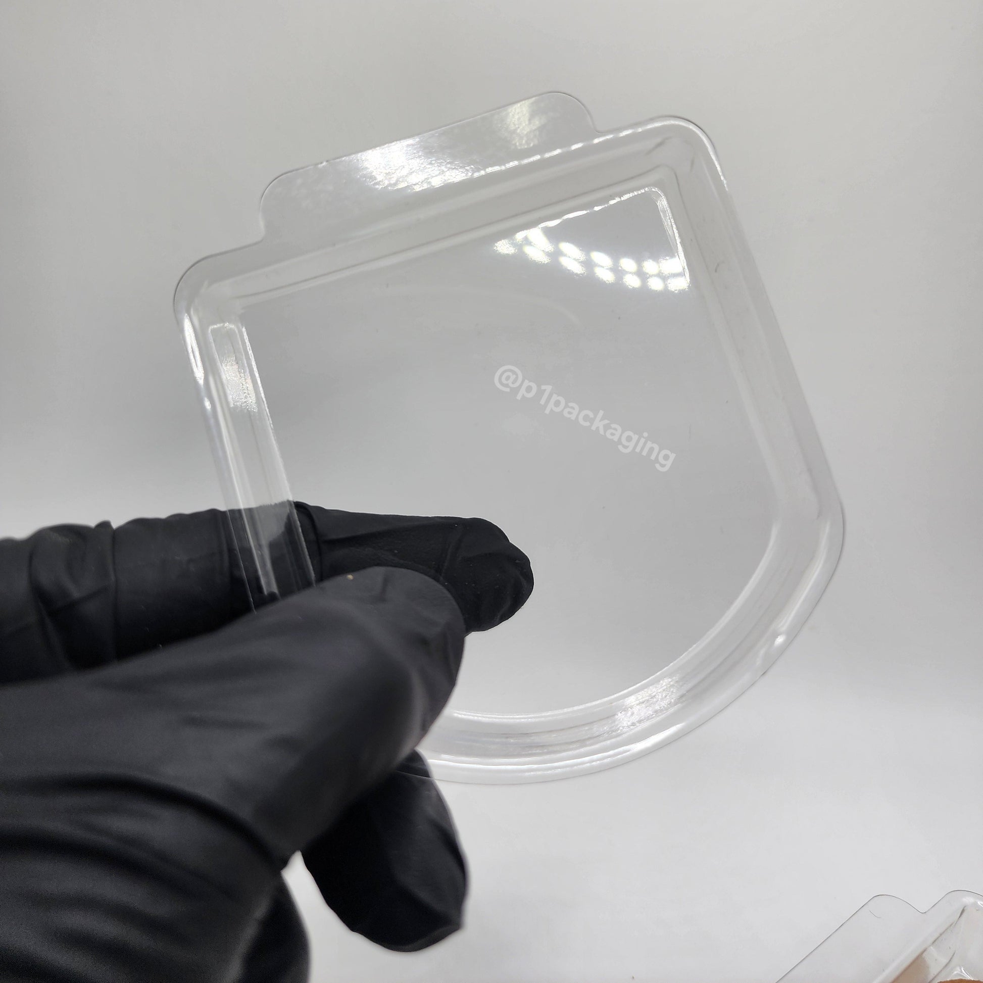Clear plastic packaging container held by a gloved hand on a white background