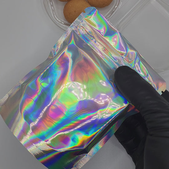 Silver holographic mylar bag and clear plastic trays with cookies inside on a white background
