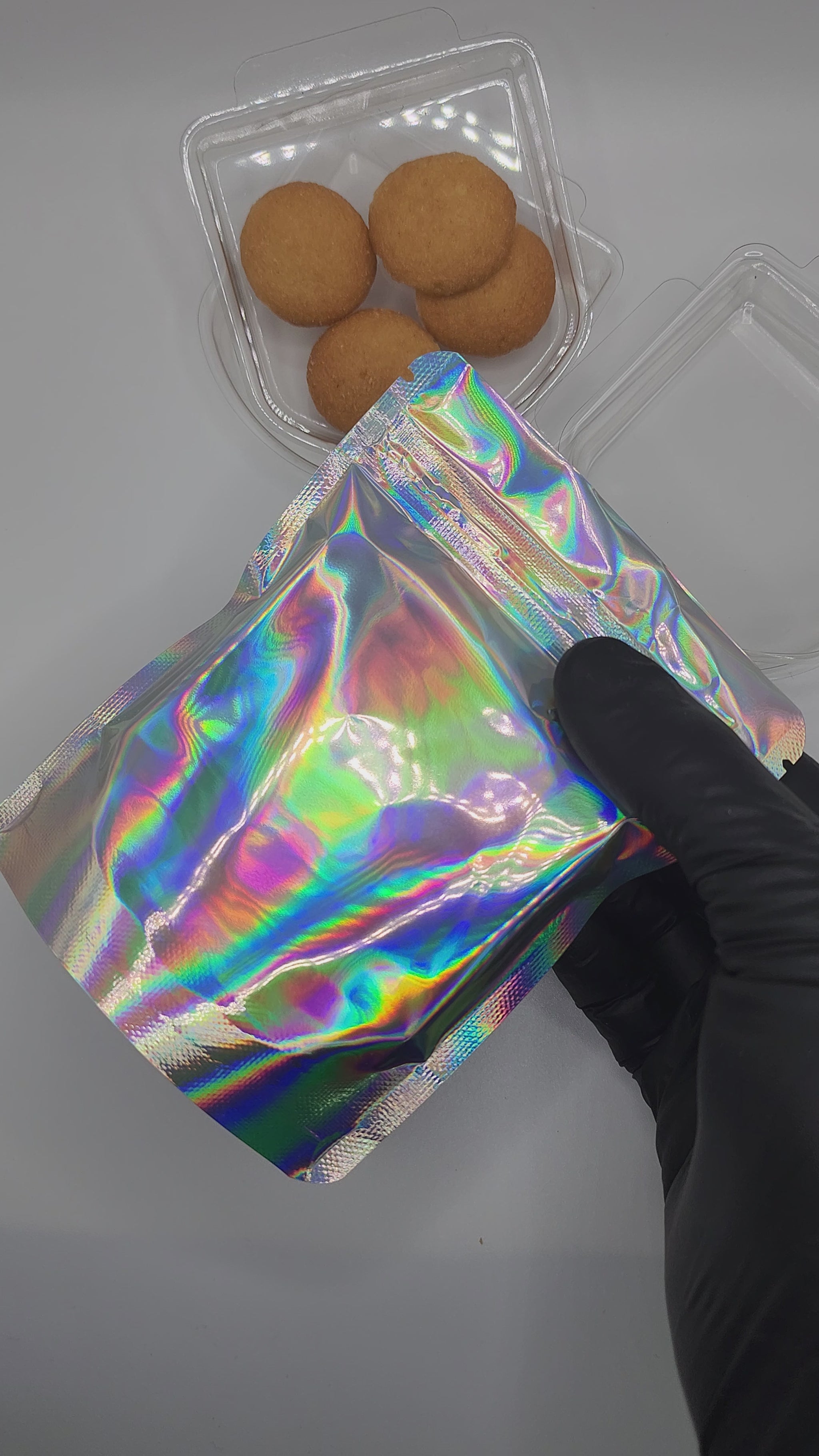 Silver holographic mylar bag and clear plastic trays with cookies inside on a white background