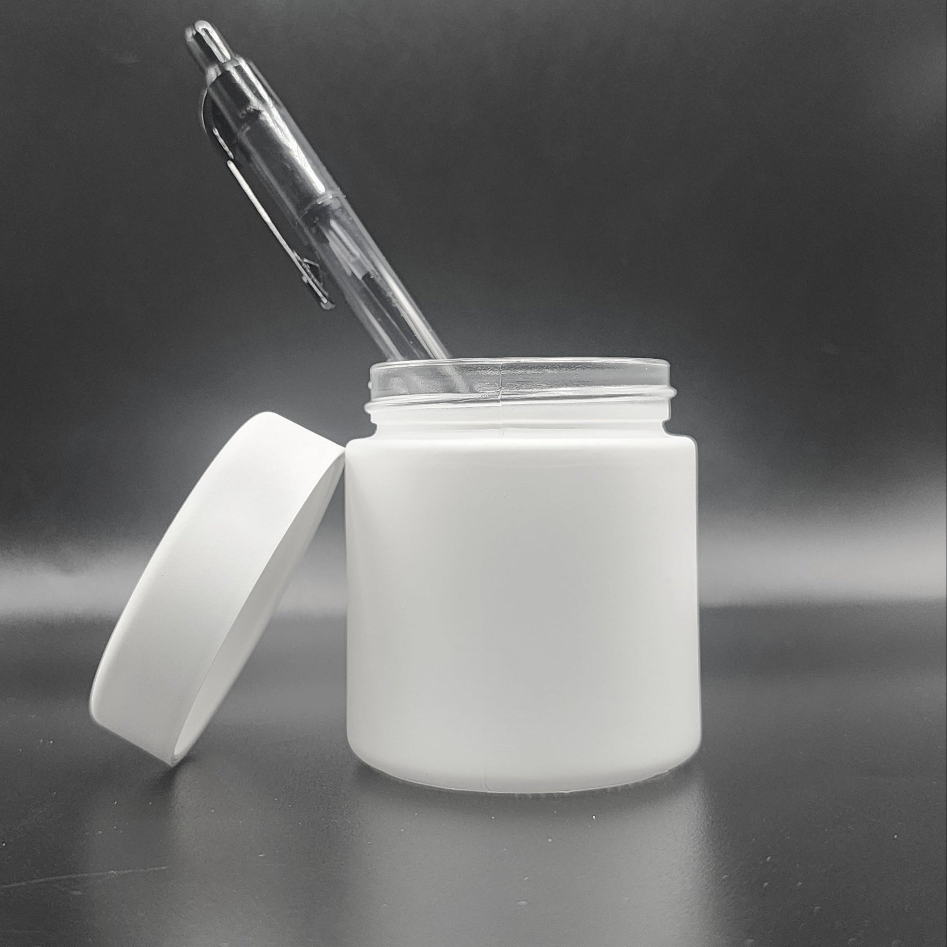 White jar with a white lid and a clear pen inside on a reflective surface with a dark background