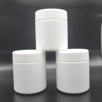 Three white cylindrical jars stacked on a reflective black surface with a blurred background