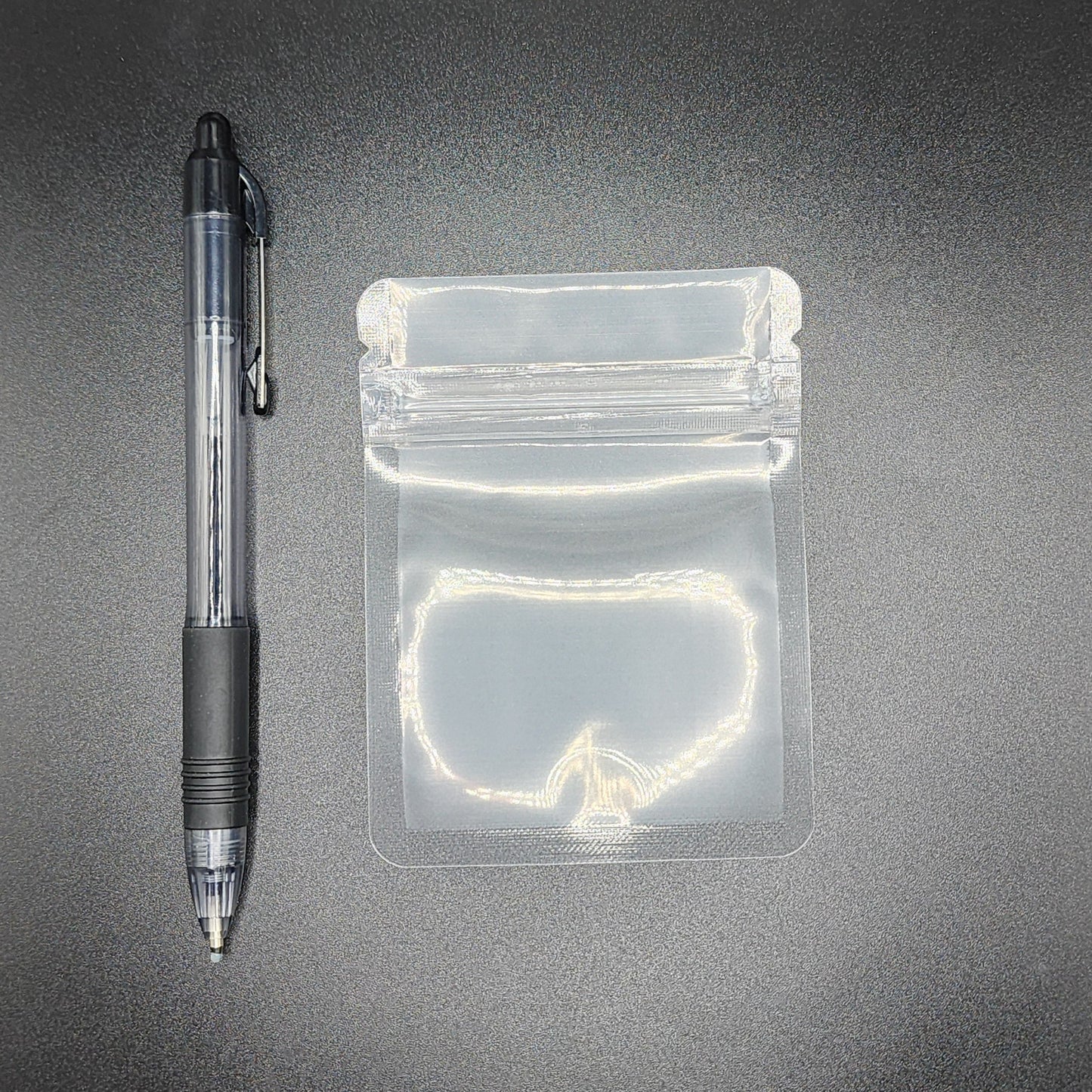 Clear 3x4 mylar bag next to a black pen on a black background