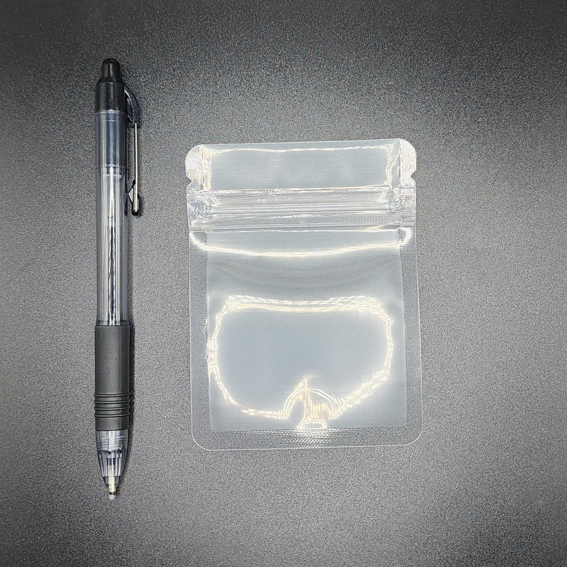 Clear 3x4 mylar bag next to a black pen on a black background