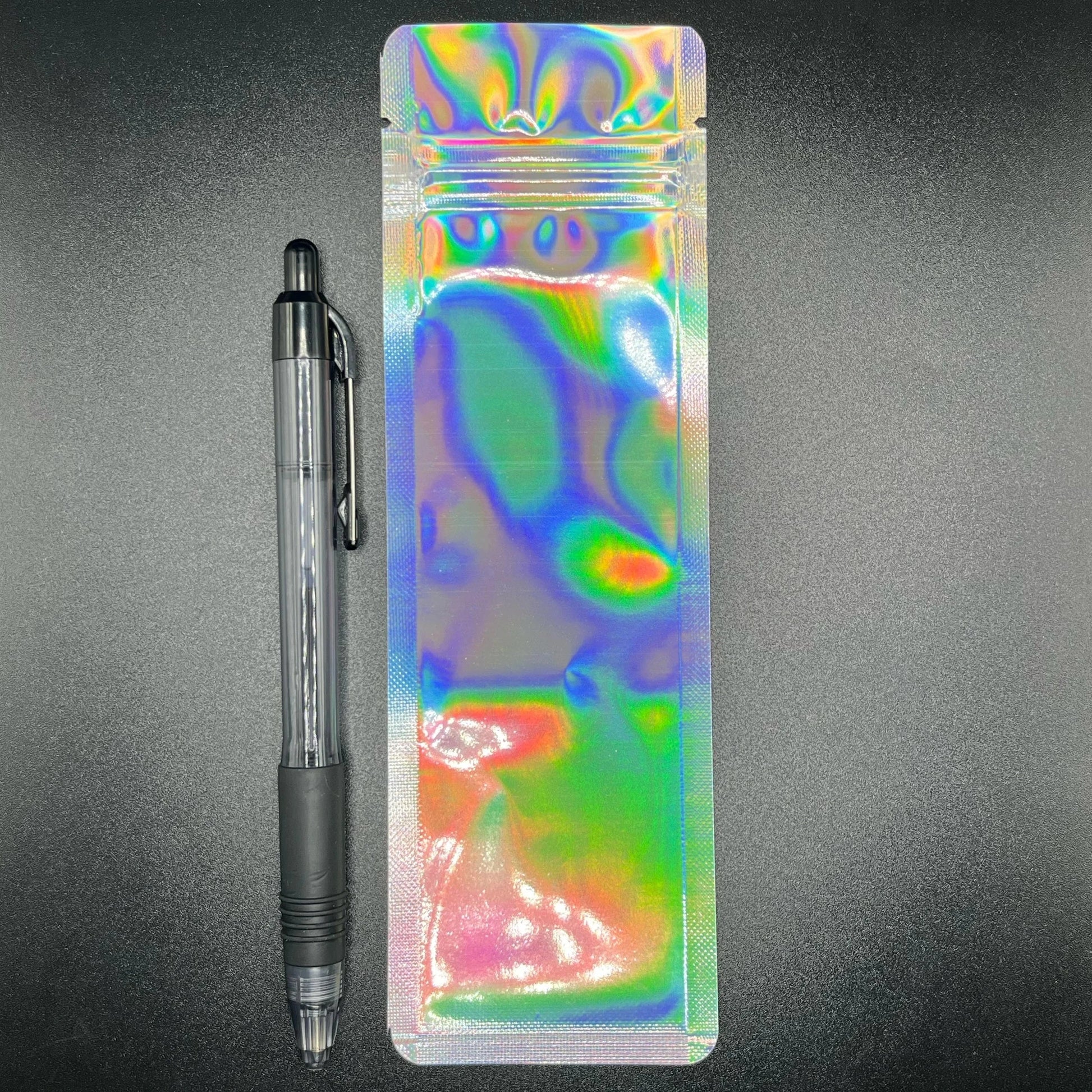 Holographic device mylar bag next to a black pen on a black background